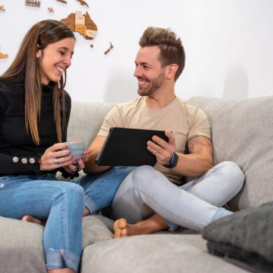 Frontal,Portrait,Of,A,Happy,Couple,Using,Tablet,Sitting,On
